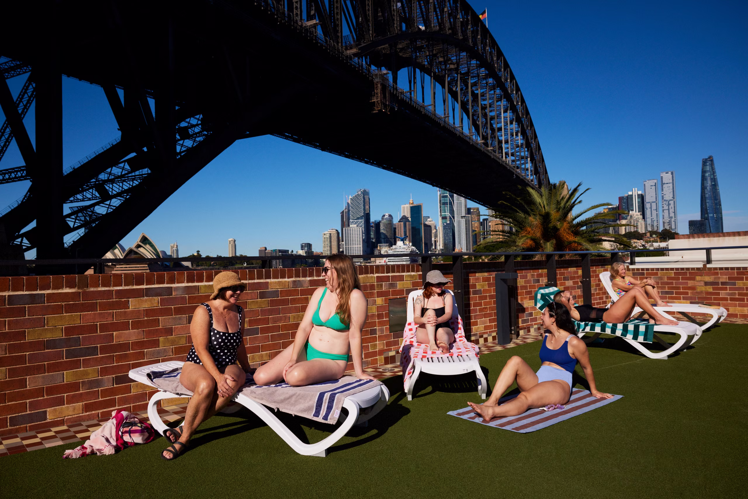 People on sun lounges on the grass beside the pool, the Harbour Bridge behind