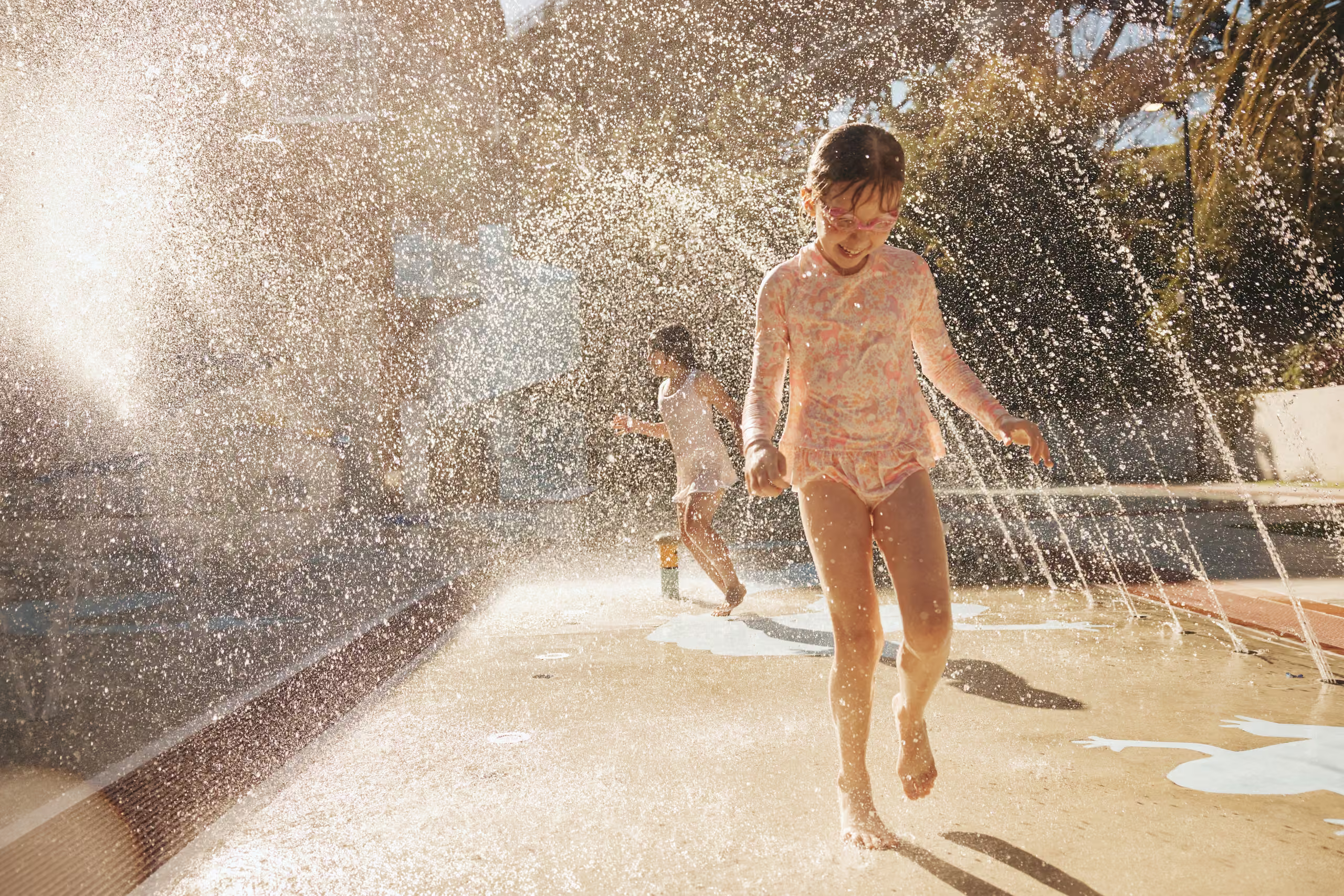A child running through the splash pad water jets in the sunshine