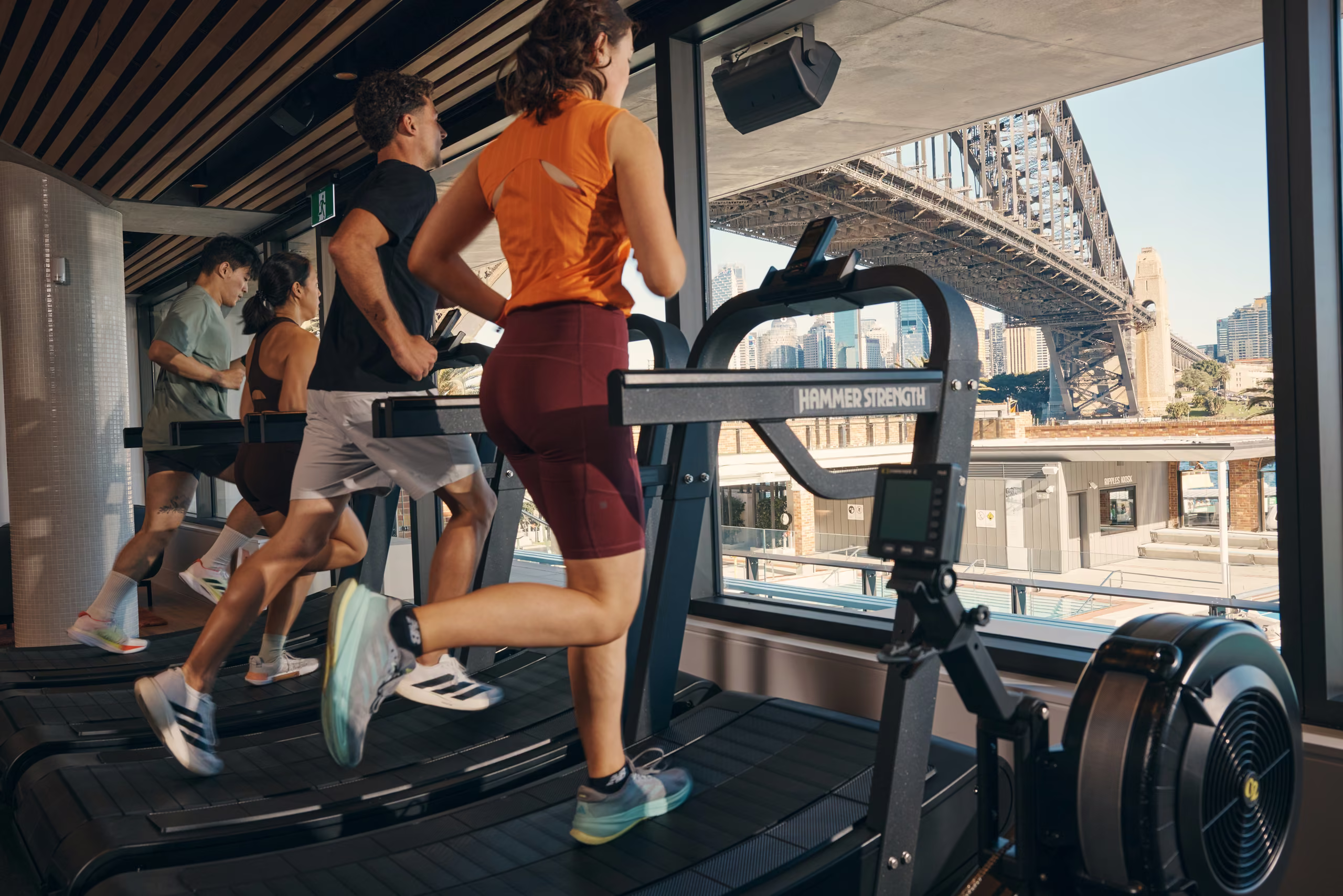 Members training on the cardio floor at North Sydney Olympic Pool, the Harbour Bridge through the window