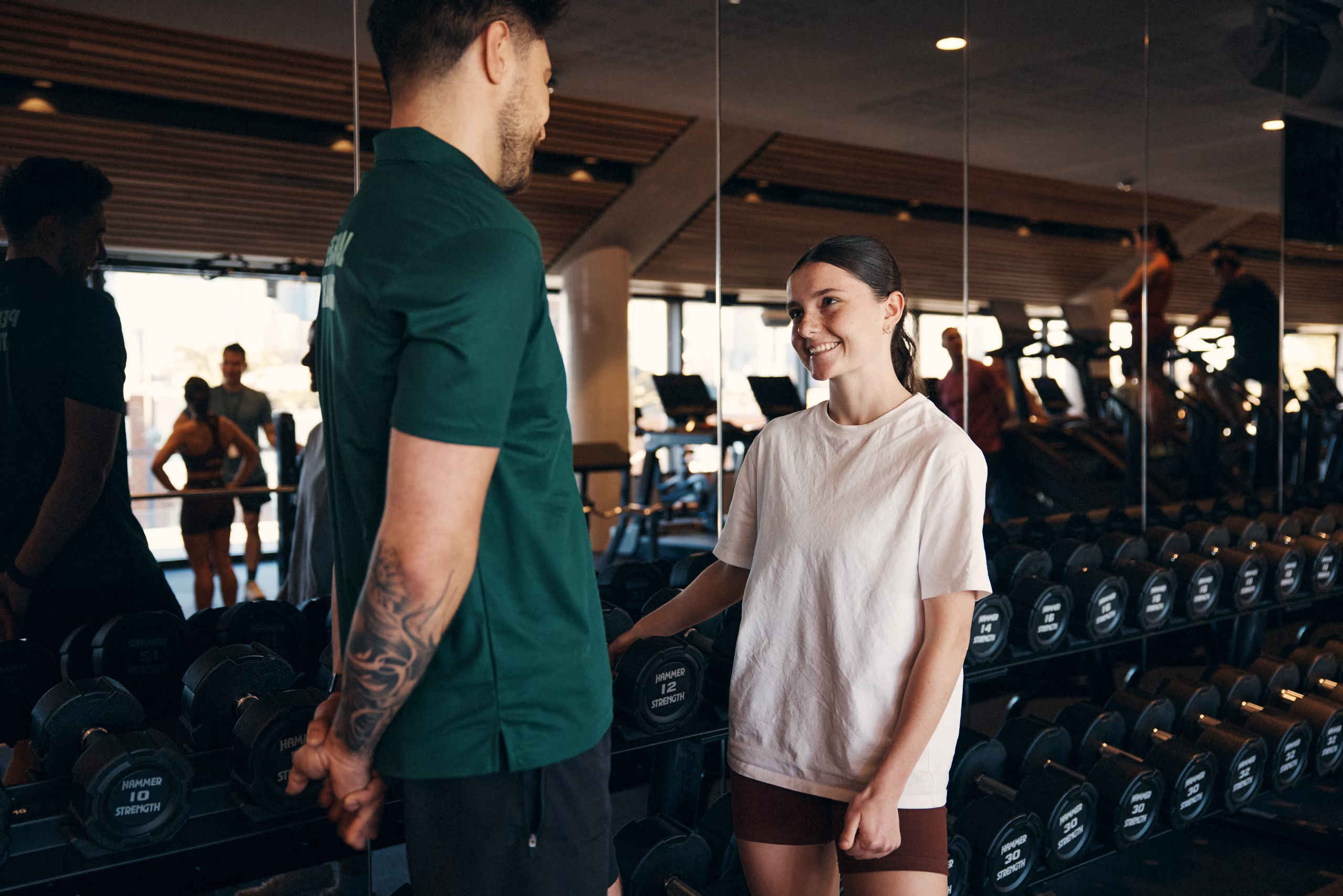 A trainer inducting a young member at the dumbbell rack
